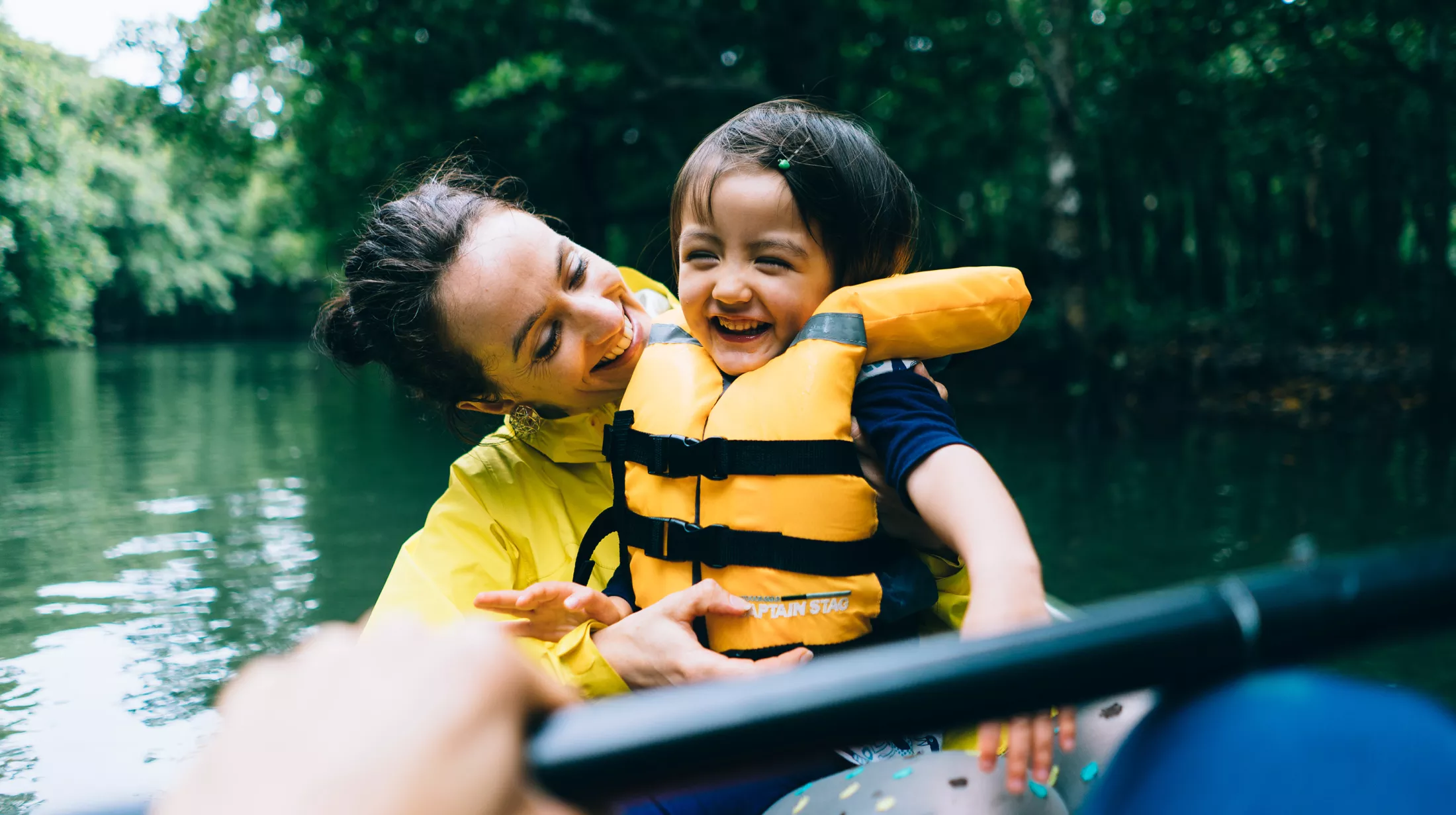 Adorable little girl laughing with her mother on kayak in mangrove forest.
