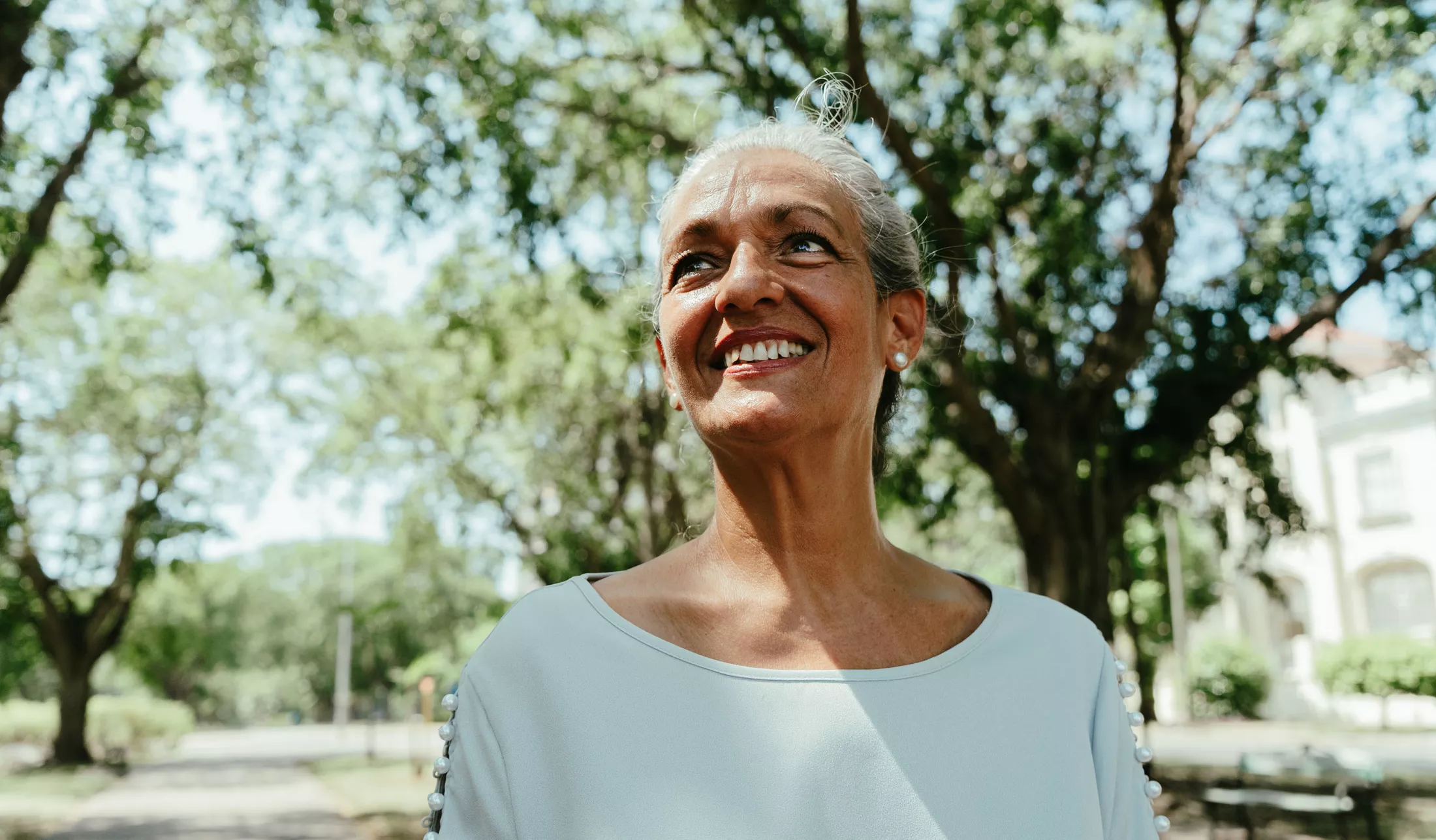 A woman outside, smiling while looking up at the sky