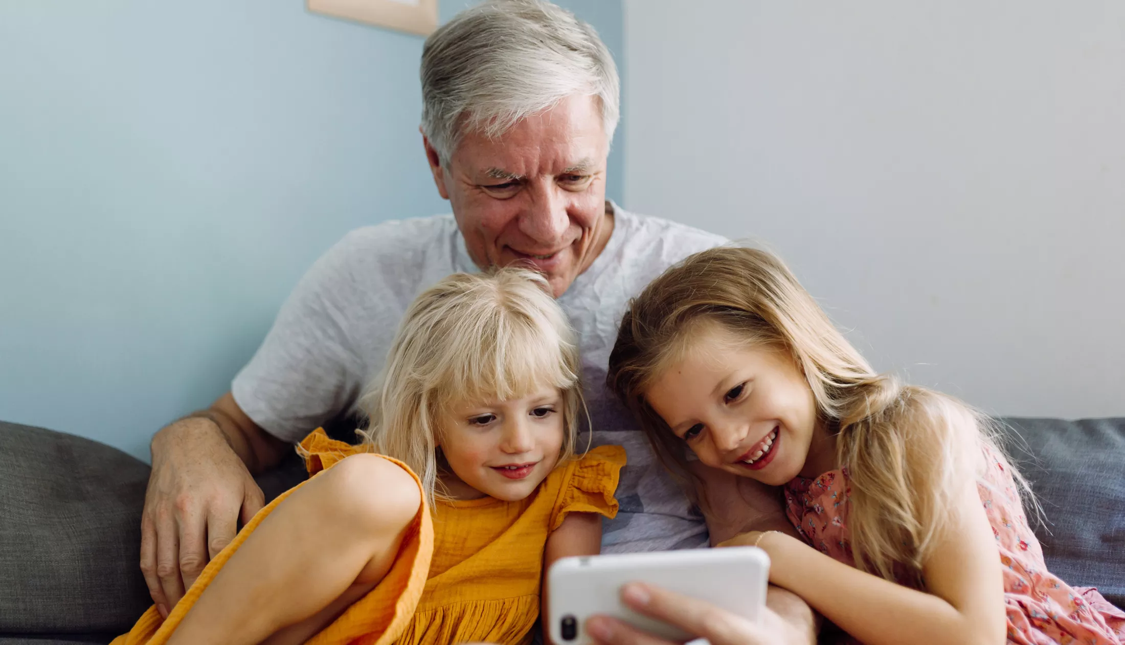 Two sisters and their grandfather laughing and having good time while using a mobile phone