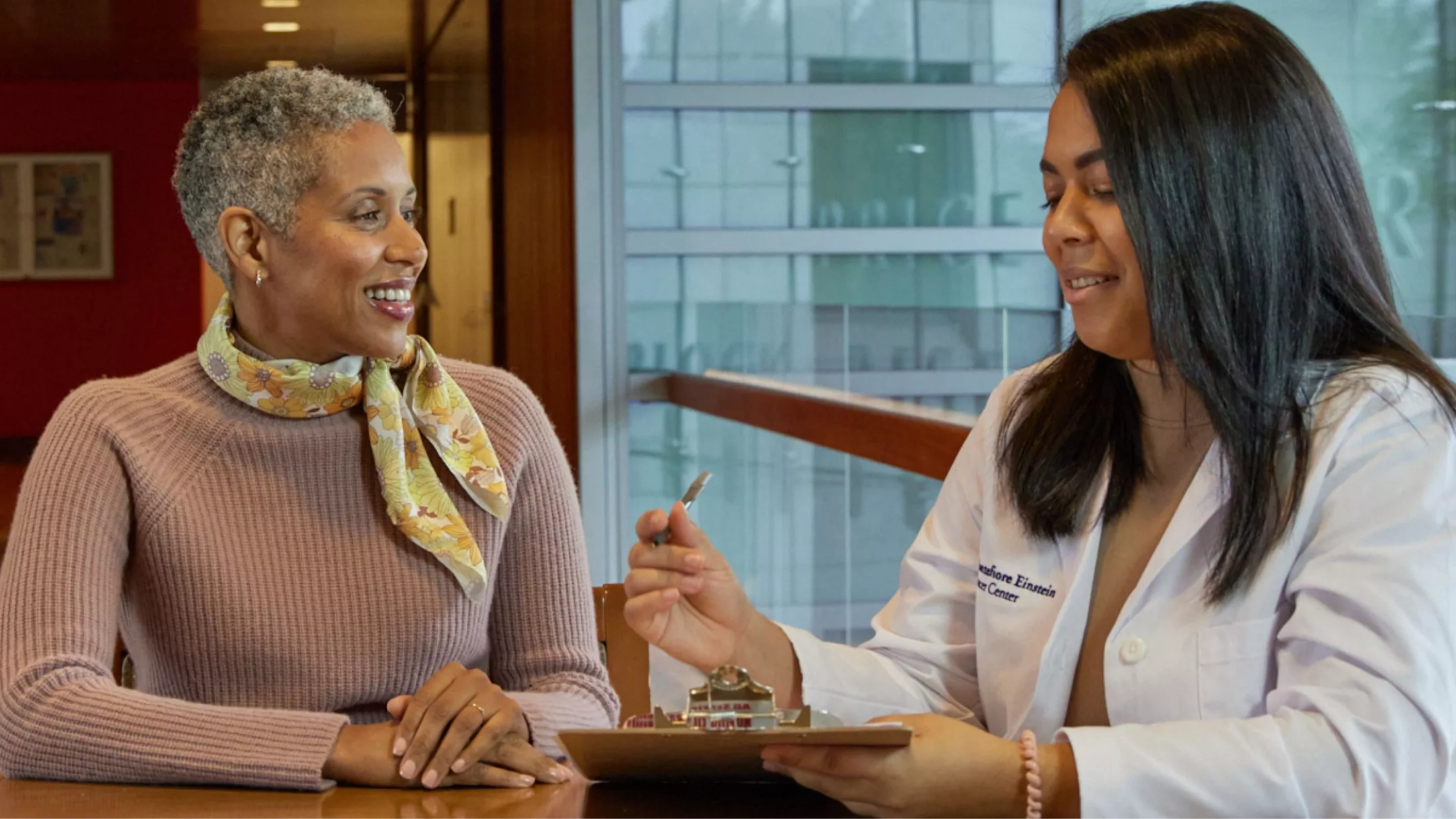 Montefiore Einstein Comprehensive Cancer Center BRONx-CAN navigator with pen and clipboard supporting a smiling patient.