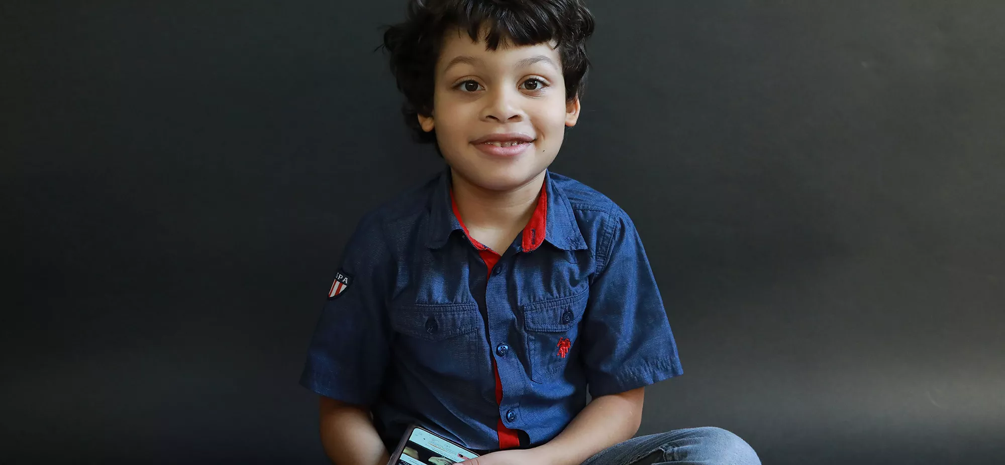 A young boy smiling while holding a mobile phone