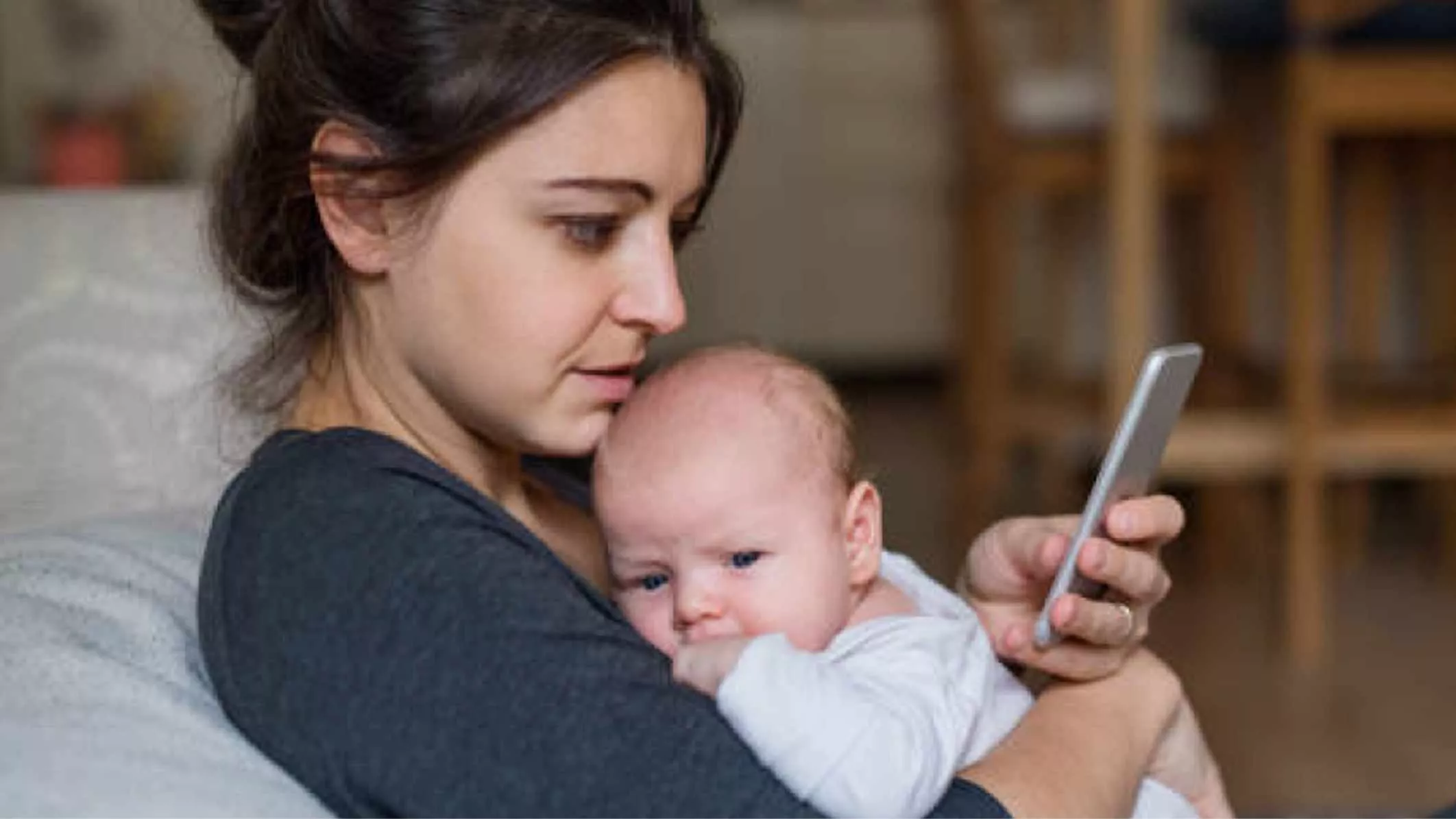Mother holding her baby while looking at cell phone