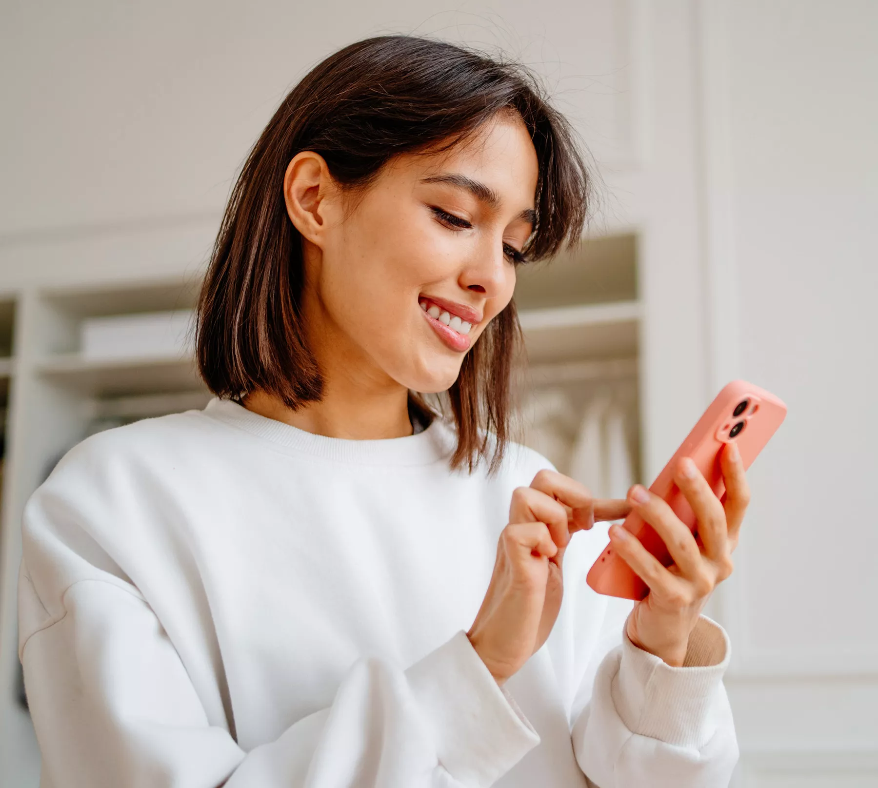 Smiling woman in a white sweatshirt using a smartphone in a bright indoor setting