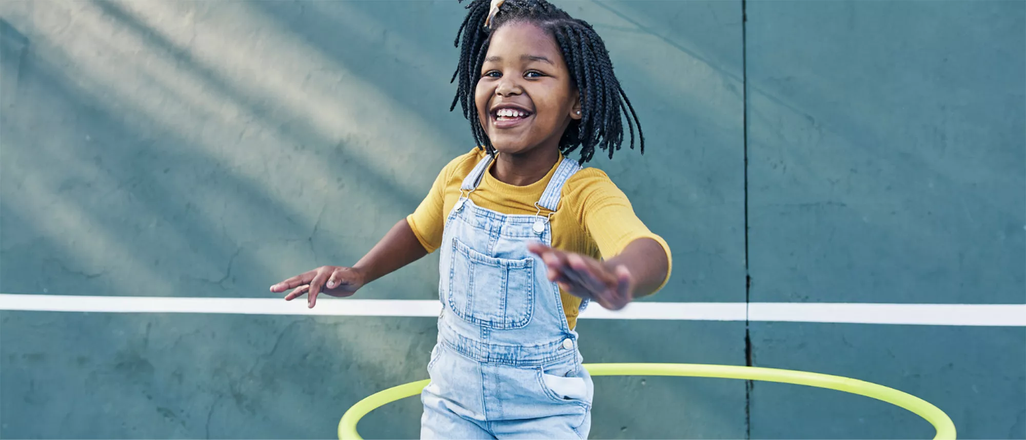 Smiling girl in overalls playing with a hula hoop on a court