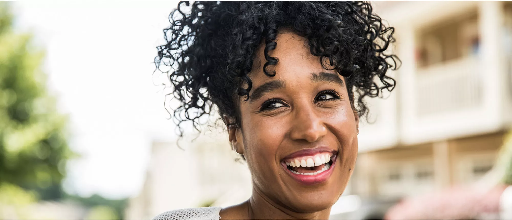Smiling woman with curly hair standing outside on a bright day