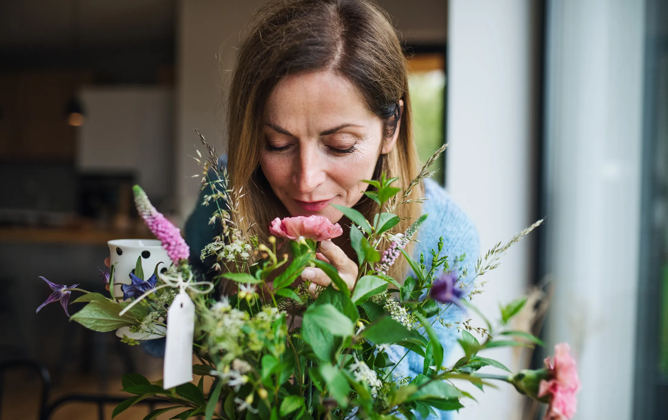 Woman smiling while smelling a colorful bouquet of fresh flowers indoors.