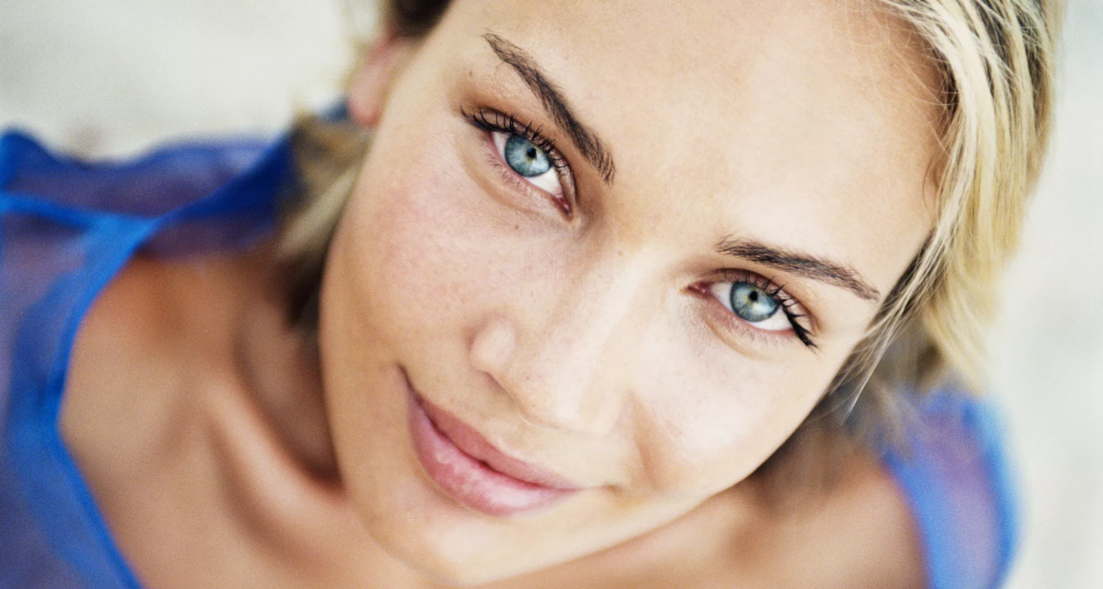 Close-up of a woman with blue eyes smiling gently while looking up at the camera