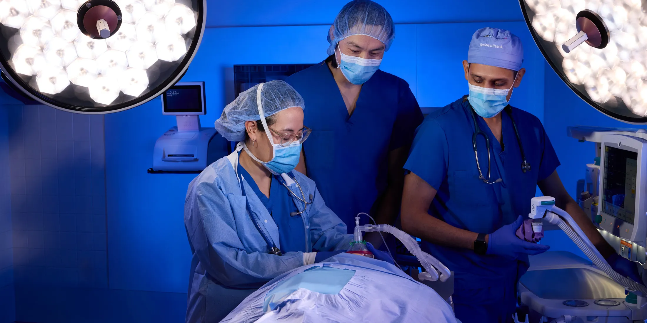 Doctors perform ultrasound on patient in blue-lit surgical suite.