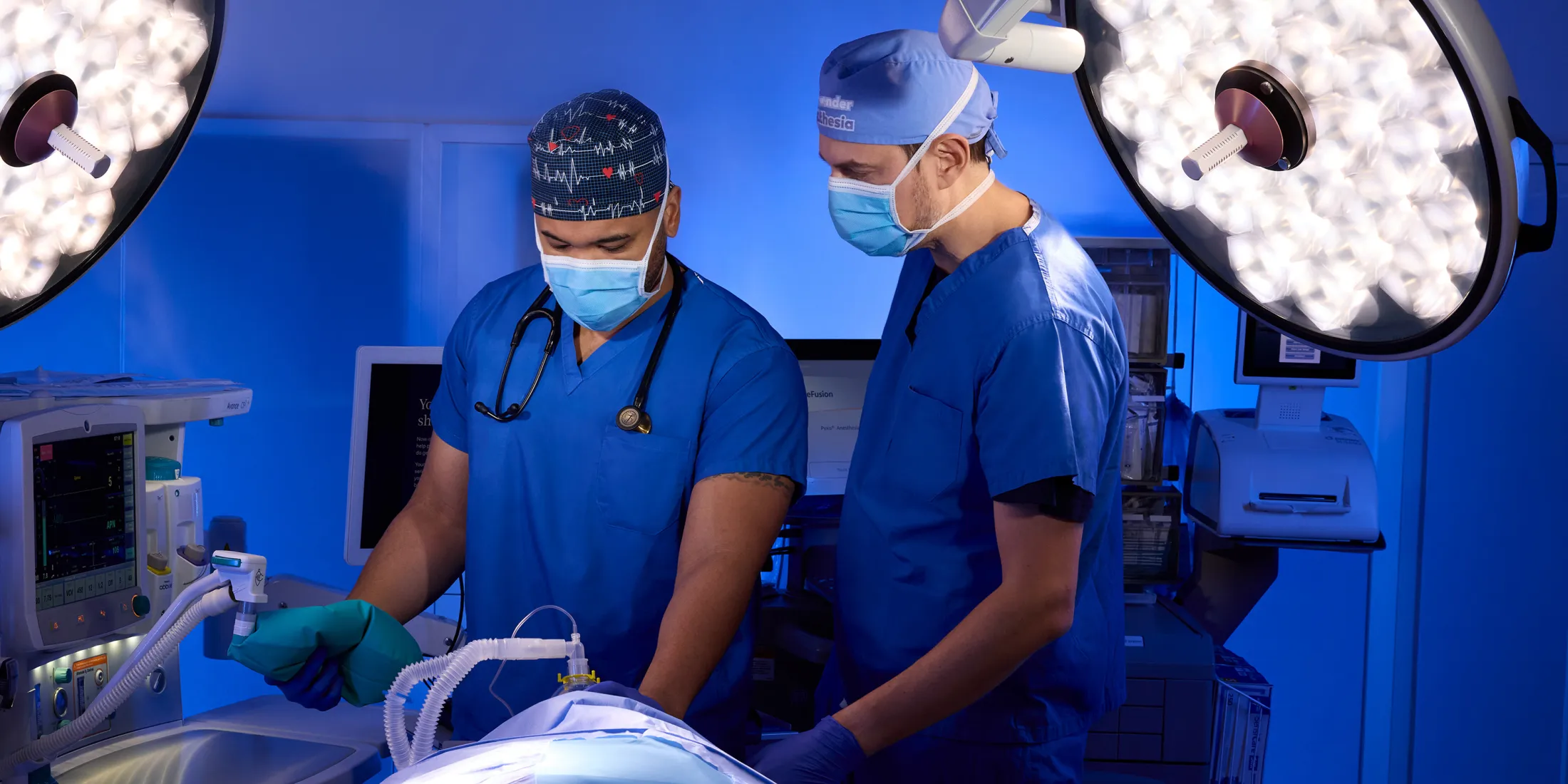 Two doctors in surgical scrubs using an anesthesia machine during an operation.