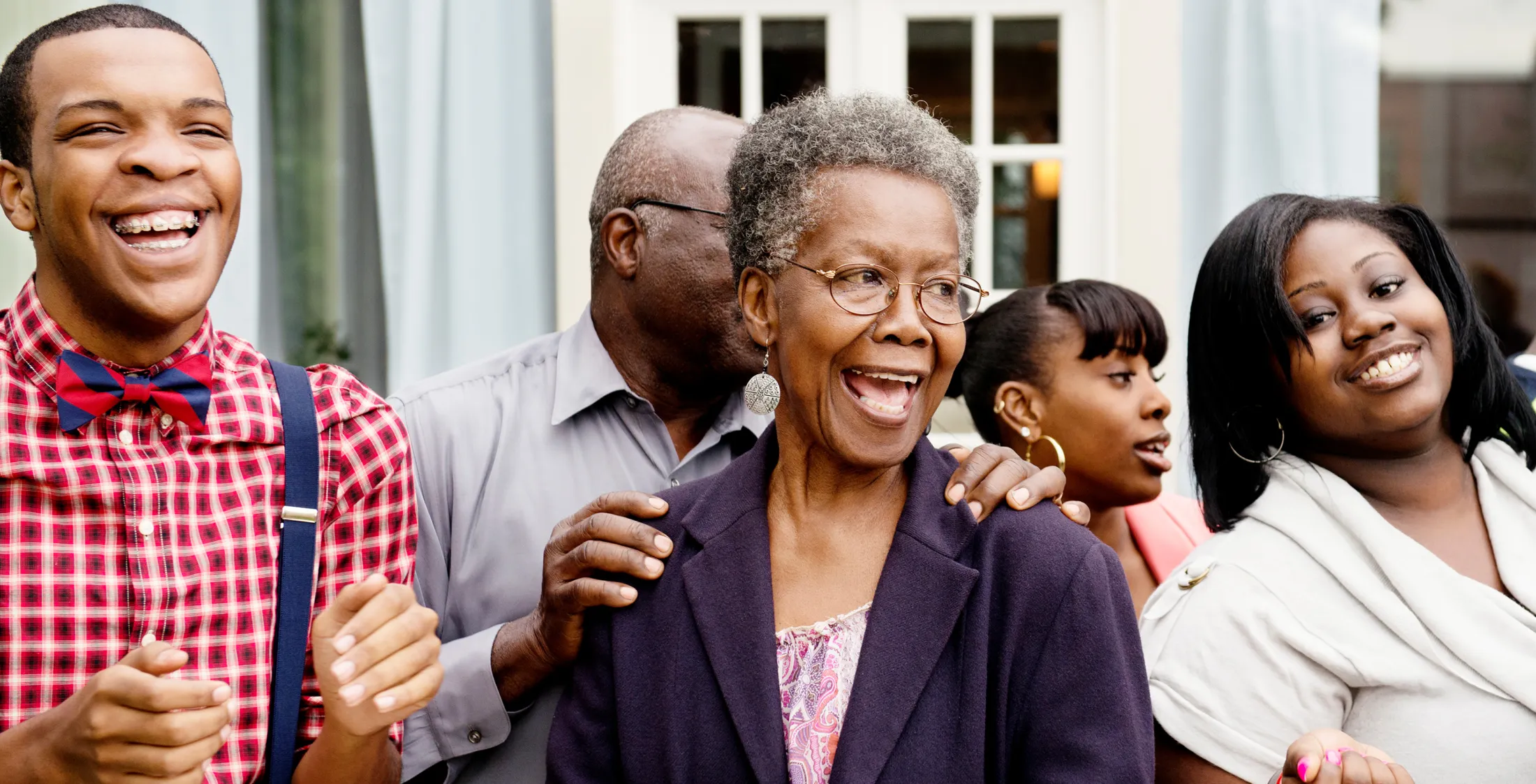 Multi-generational family standing together outdoors, smiling and laughing during a joyful moment.