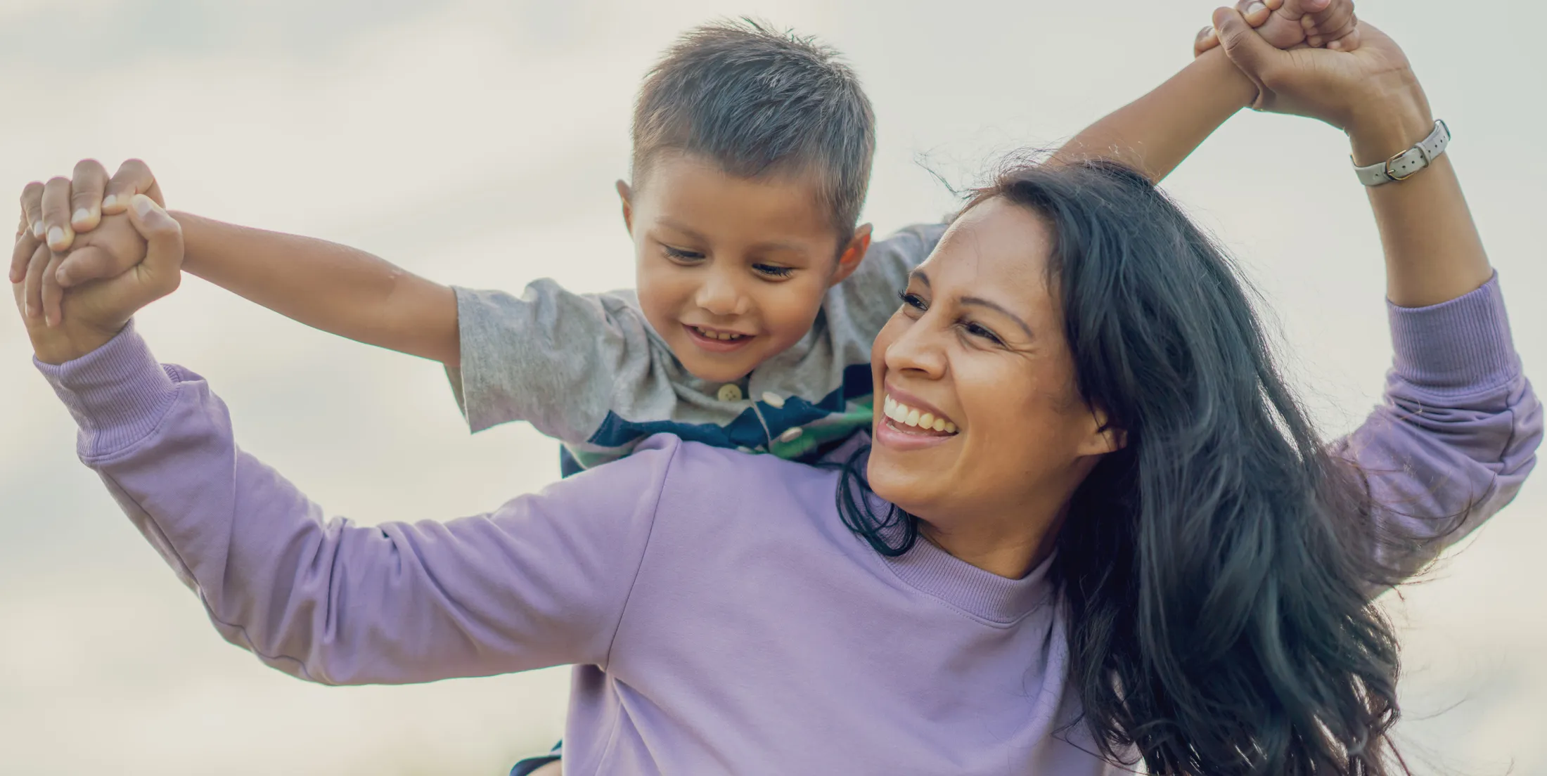 Happy mother giving her young son a piggyback ride while holding hands outside