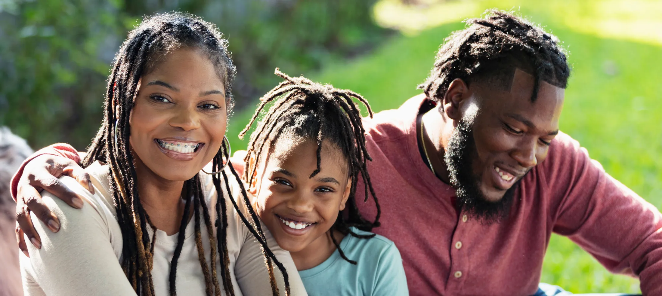 Family with parents and child smiling and sitting on the grass in a park.