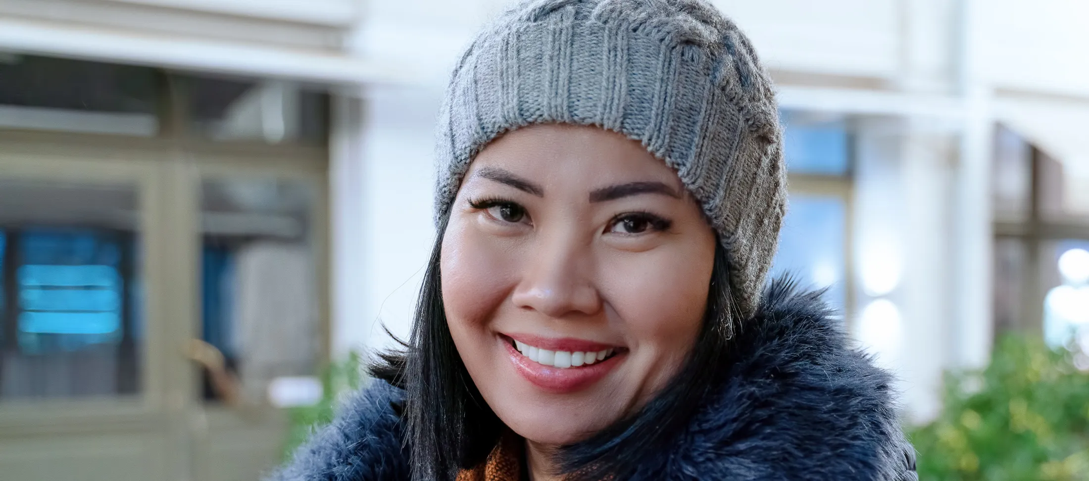 Smiling woman in a knit hat and winter coat standing outside in a city setting