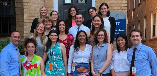 Group of faculty and interns posing together outside a brick building with a Montefiore sign.