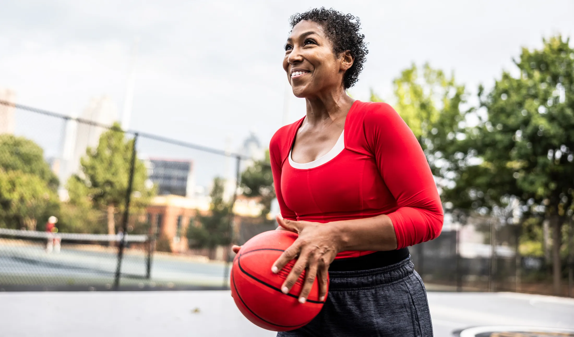 Woman holding a basketball and smiling on an outdoor basketball court.