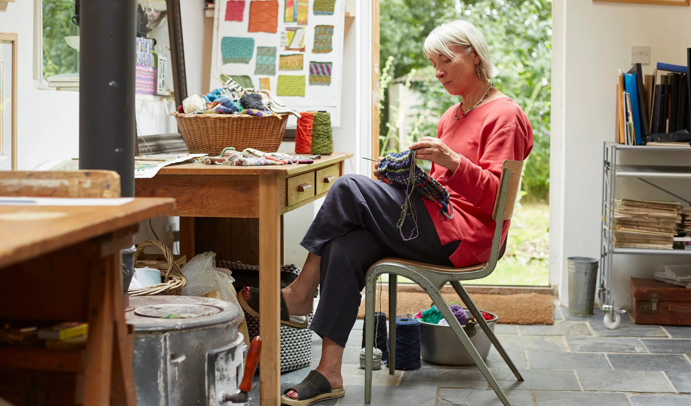 Woman in red knitting by a window in a cozy craft room