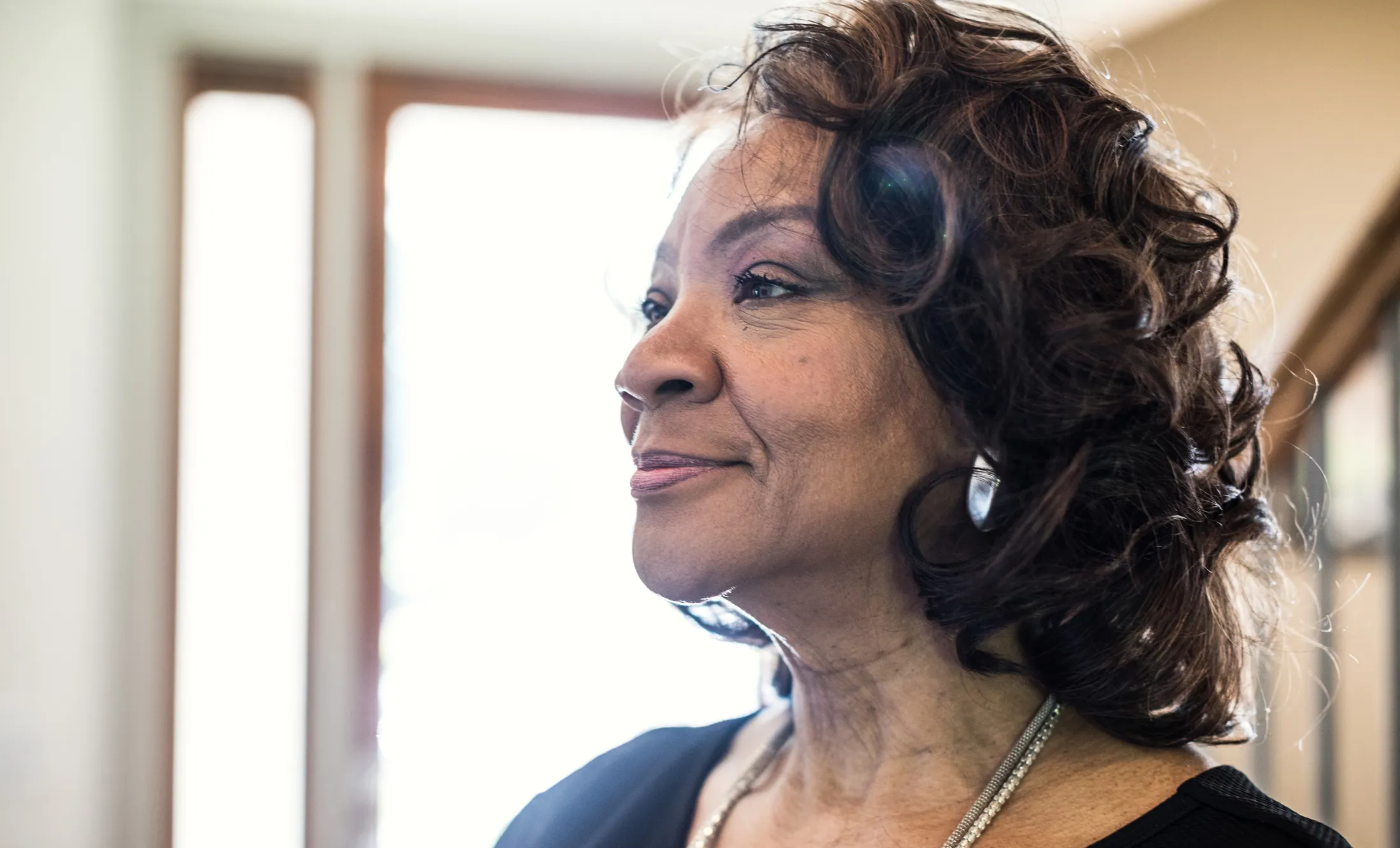 Older woman smiling in soft natural light with a thoughtful expression.