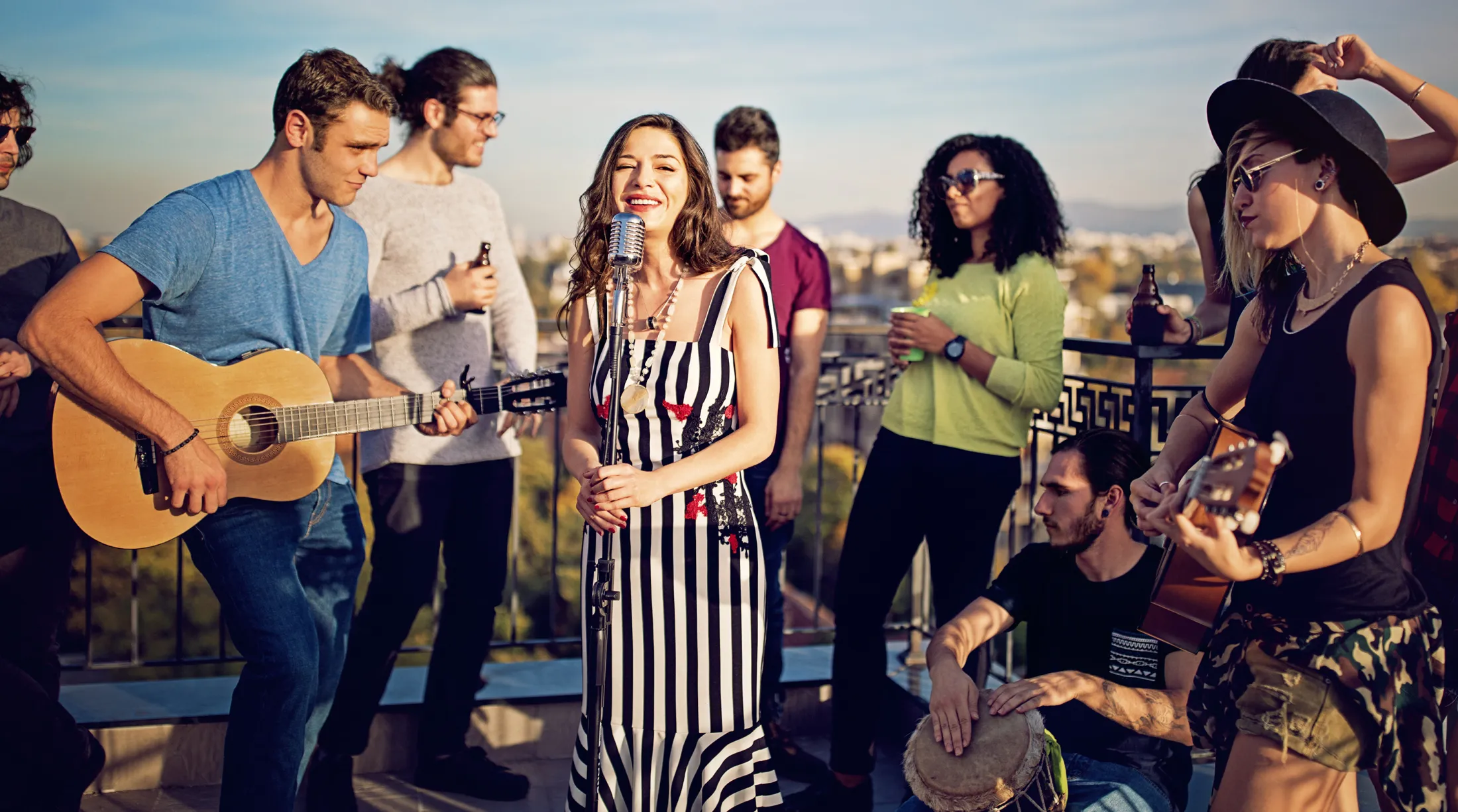 Group of friends playing music and singing together at a rooftop party during the day.