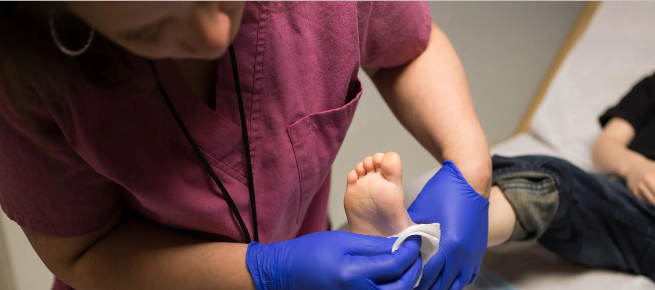 Nurse dressing up a foot wound of a young child lying in bed.