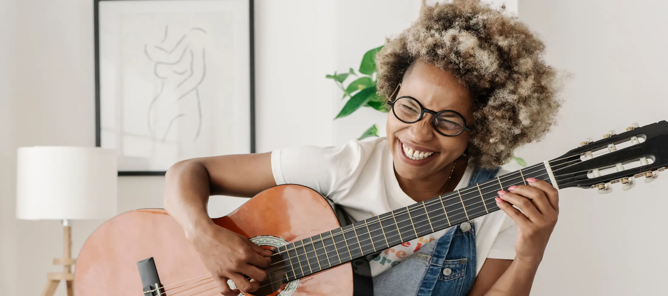 Woman wearing glasses and playing a guitar while smiling