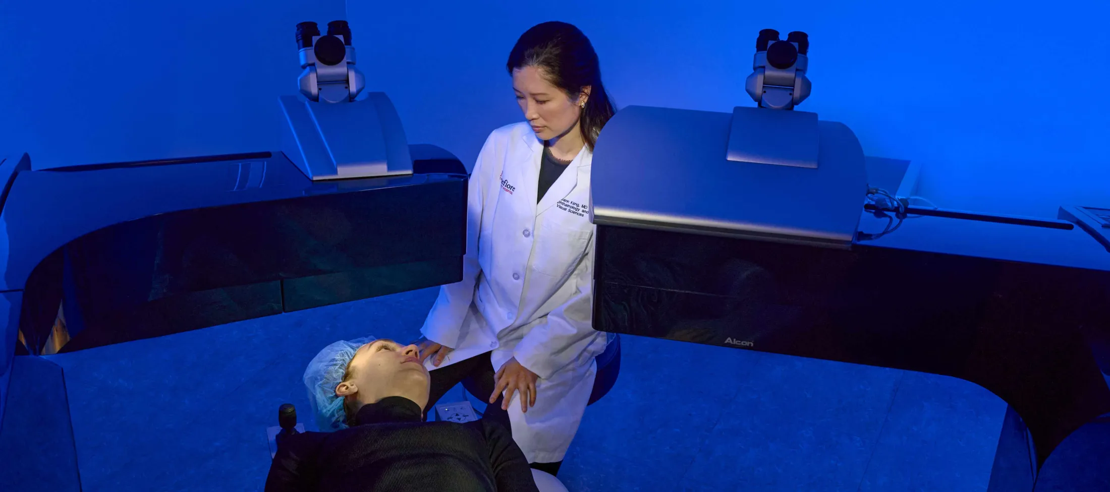 Patient laying down on the operating table talking to a doctor in a laser eye surgery blue room