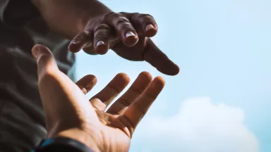 Two hands extending toward one another against blue sky.