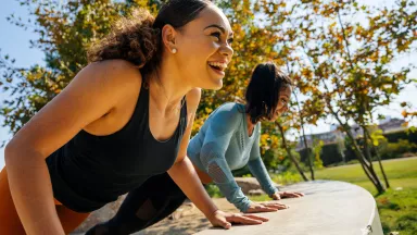 Cheerful women doing push-ups on retaining wall at park
