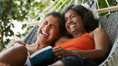 Two women reading a book in a hammock 