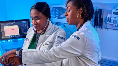 Two medical professionals in lab coats collaborate while using medical equipment in a high-tech clinical setting.