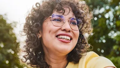 Woman wearing glasses with a big smile with trees in the background.