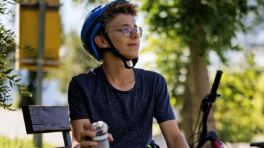 Boy on bicycle wearing eye-glasses looking far away