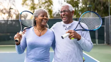Man and woman holding tennis rackets laughing.