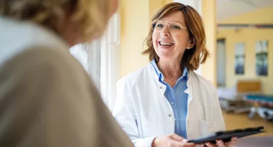 A smiling senior doctor with a digital tablet talking to a female patient at a hospital. 