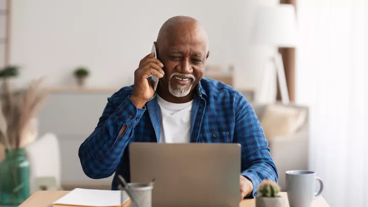 A man talking on cellphone using laptop in office.