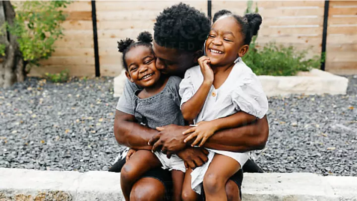 A father embracing his two smiling daughters outside