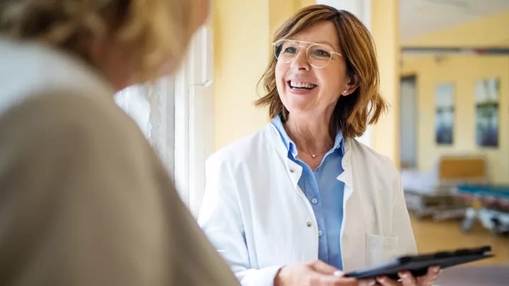 A smiling senior doctor with a digital tablet talking to a female patient at a hospital. 