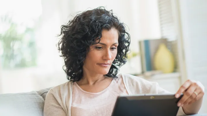 Woman sitting on a couch at home, focused while using a digital tablet in a well-lit living room