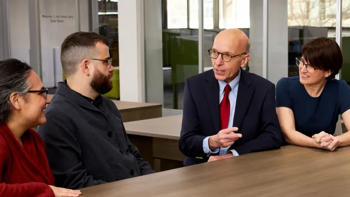 Four colleagues having a discussion around a wooden table in a modern office space