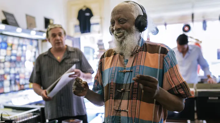 Elderly man smiling while listening to music on headphones in a record store.
