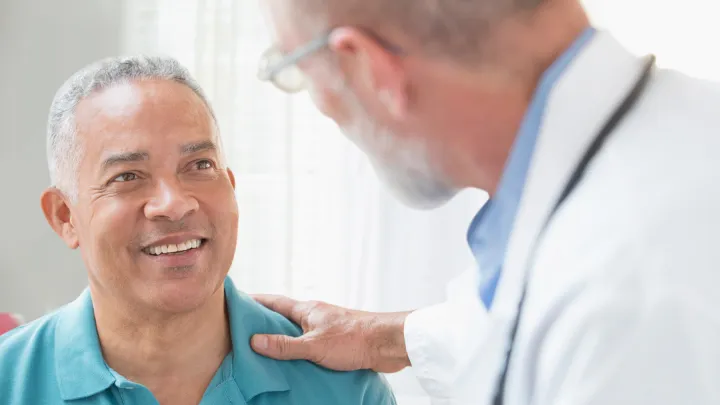 Middle-aged man smiling at a doctor who rests a reassuring hand on his shoulder.