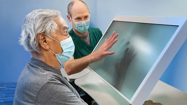 Clinician guiding an elderly patient using an interactive touchscreen for hand rehabilitation exercises.