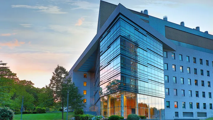 Modern glass-fronted academic or medical research building surrounded by trees at sunset.