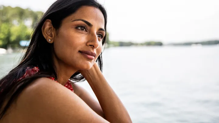 Thoughtful woman gazes into the distance while relaxing outdoors near a calm body of water.