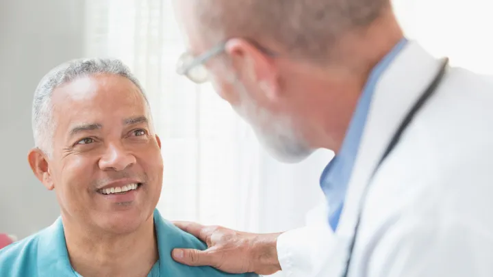 Middle-aged man smiling at a doctor who rests a reassuring hand on his shoulder.
