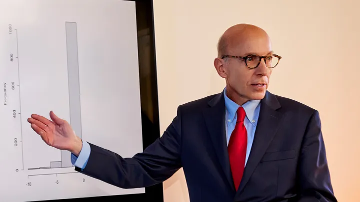 Professional man in a suit and red tie presenting data on a large screen with a frequency graph.