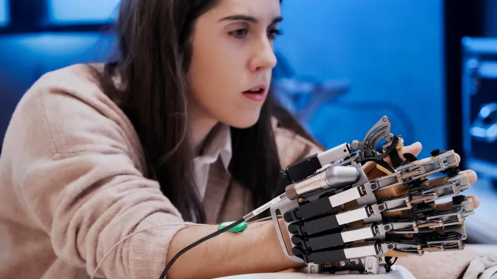 Researcher tests a robotic exoskeleton hand device attached to their arm in a lab setting