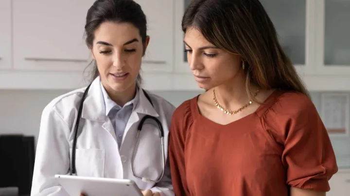 A female doctor explaining something to a female patient, using a tablet