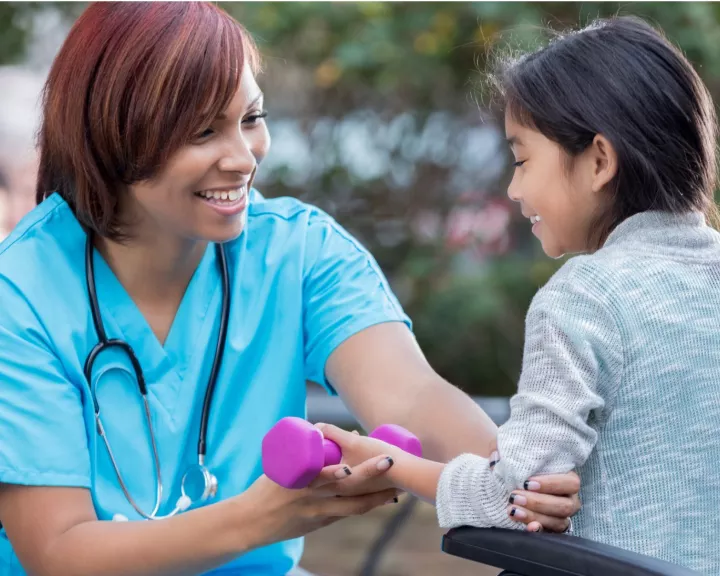 Smiling nurse assists young girl with exercising in wheelchair