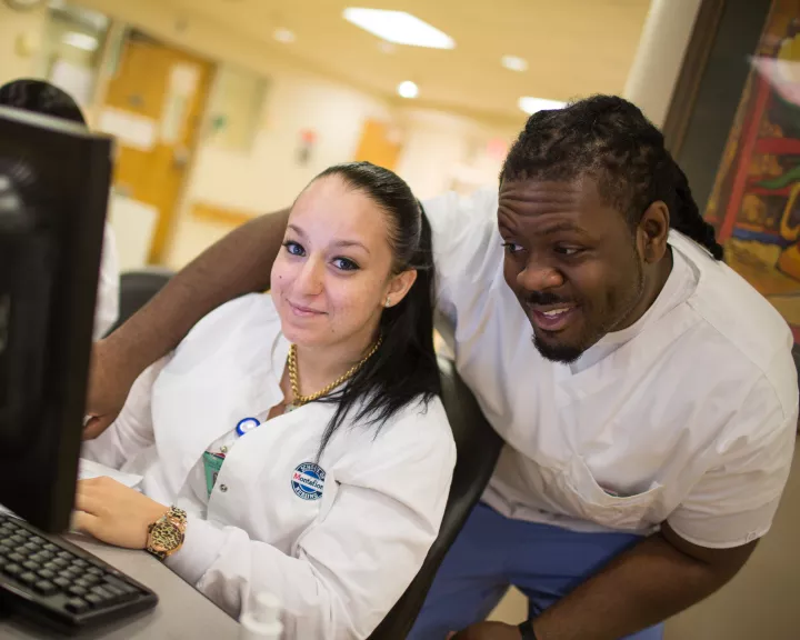 Two nursing students smiling at desk looking at display