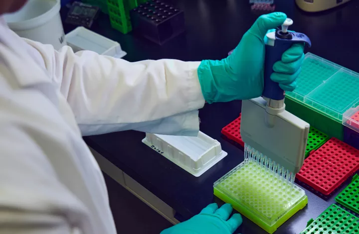 Scientist in lab coat using pipette to measure sample in laboratory.